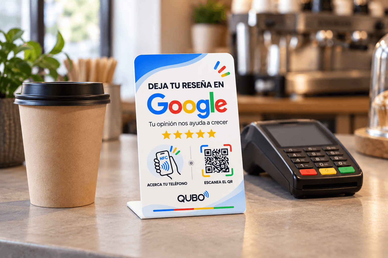QUBO Tap blanco en el mostrador de una cafetería, entre un vaso de café y un datáfono, más bajo que el vaso